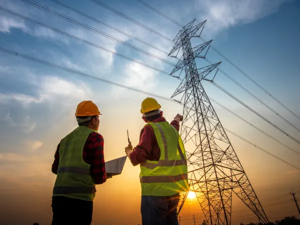 Electrical power transmission engineers inspecting a high-voltage transmission tower and power lines.