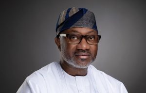 Portrait of Femi Otedola, the Nigerian billionaire invests in Dangote Refinery, wearing traditional white clothing and a blue patterned cap against a grey background.