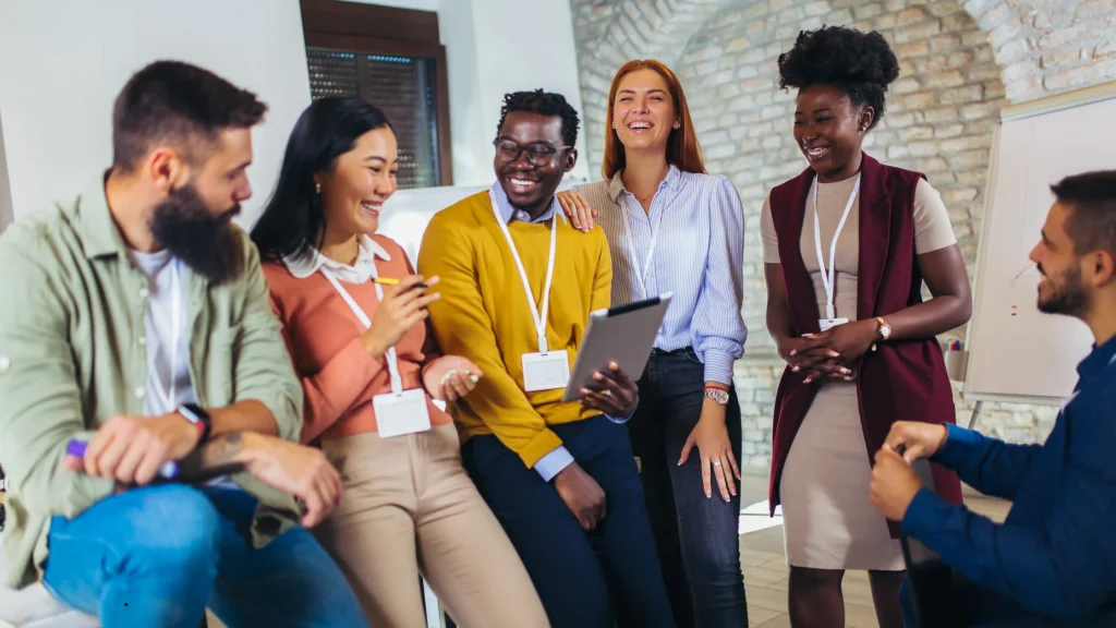 A diverse group of happy young professionals collaborating and looking at a tablet during an office workshop, showcasing effective talent management and team engagement.