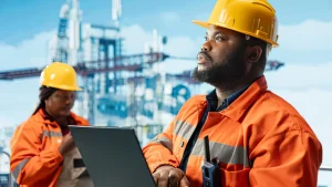 Offshore oil and gas engineers in safety gear managing crew logistics on a laptop, demonstrating comprehensive offshore support services