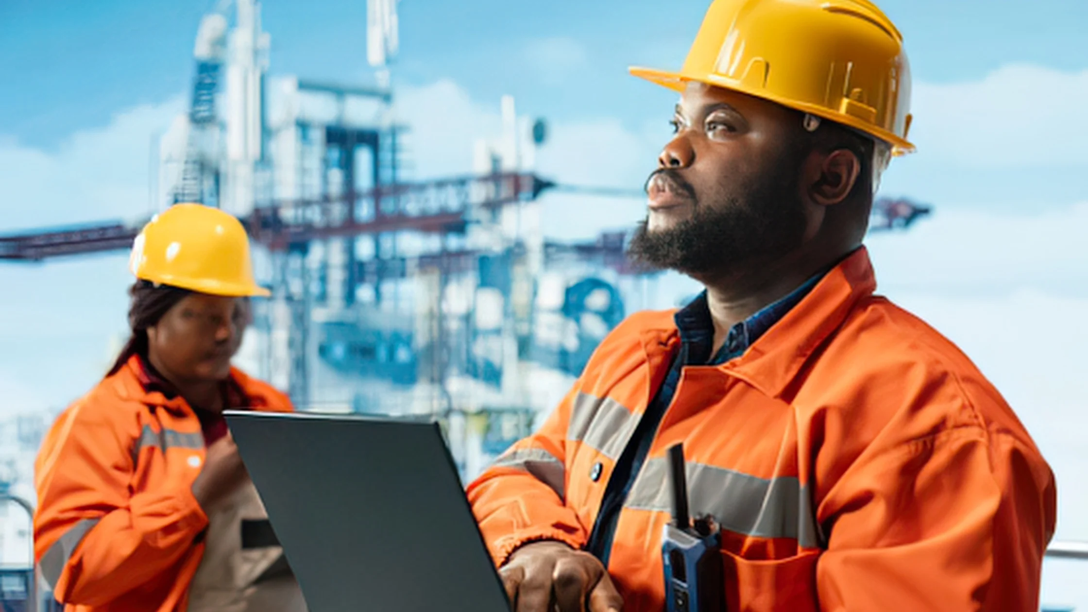 Offshore oil and gas engineers in safety gear managing crew logistics on a laptop, demonstrating comprehensive offshore support services