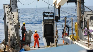 Offshore workforce management in action as crew members operate heavy crane machinery on the deck of a vessel at sea