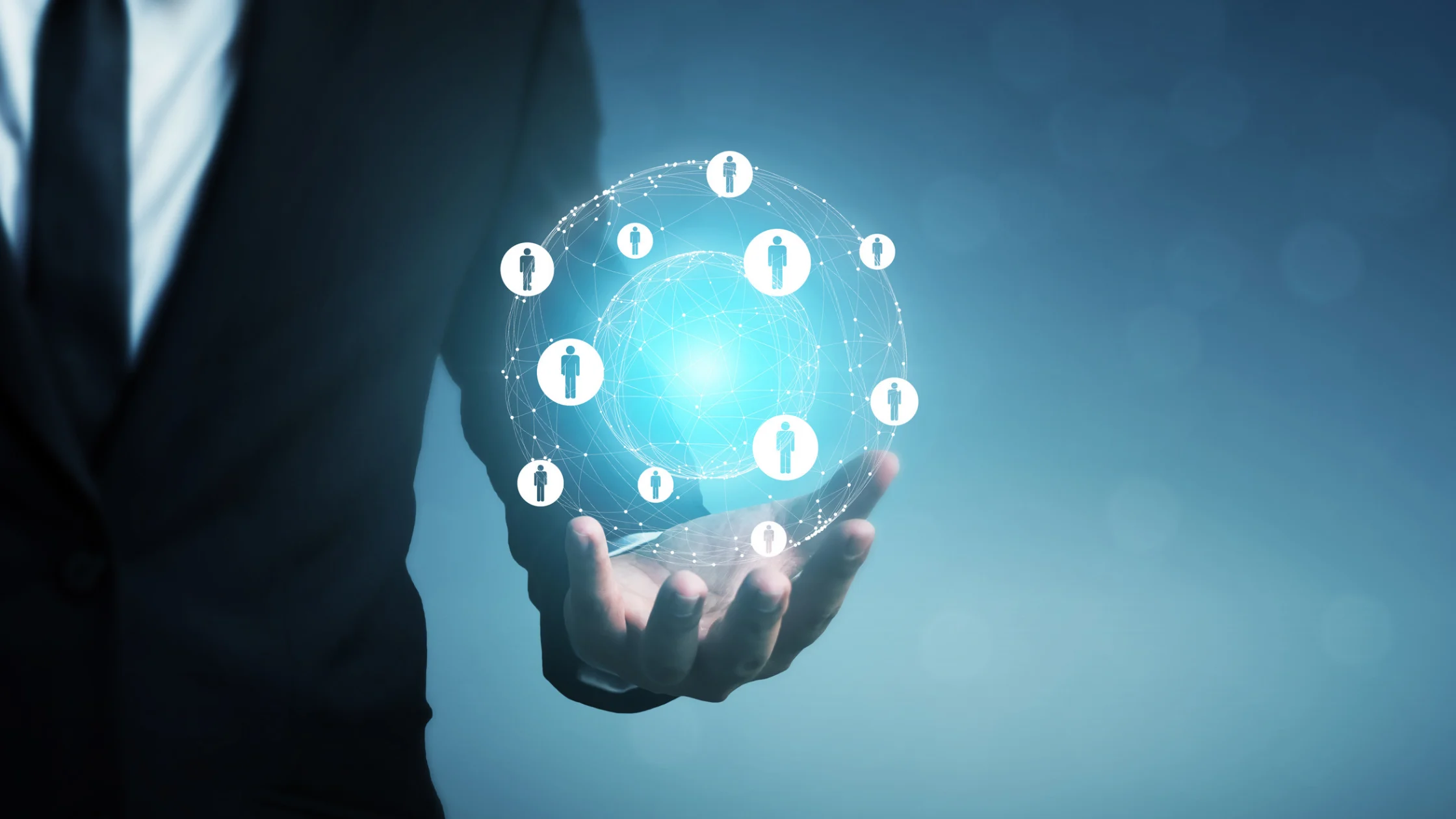 A businessman in a suit holding a glowing digital globe surrounded by interconnected human profile icons, representing a modern global talent management strategy and international HR network.